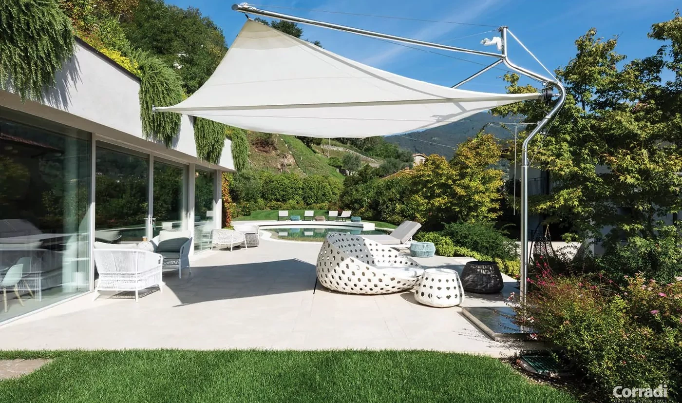 In passend modernem Stil beschattet ein Corradi Defense Sonnensegel Sitzgelegenheiten einer Terrasse mit Pool neben einem modernen Haus in den Bergen.