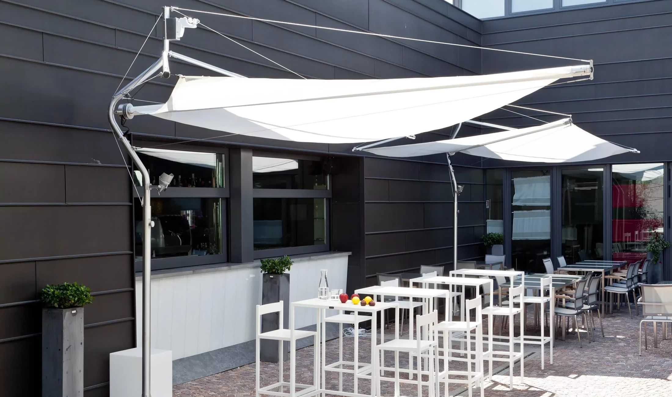 Zwei Corradi Sun Sail Defense als Sonnenschutz für den Außensitzbereich in der Gastronomie.