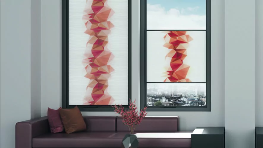 Zwei Fenster mit Wabenplissees von MHZ mit einem Design geometrischer Formen in Rottönen. Das eine Fenster wird voll verdeckt, das andere zur Hälfte.