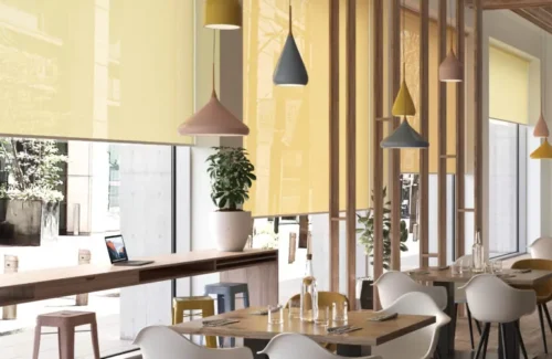 Mehrere gelbe Rollos schützen ein Restaurant vor Sonnenlicht und setzen gleichzeitig farbliche Akzente in dem Raum.