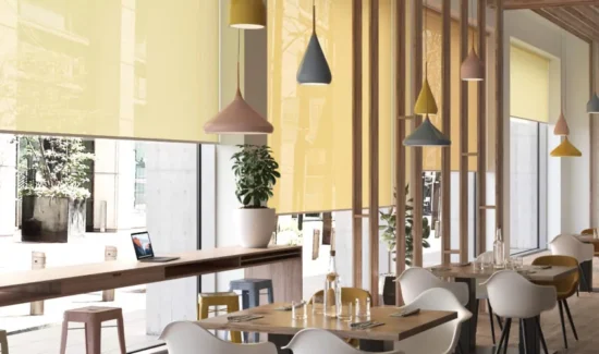 Mehrere gelbe Rollos schützen ein Restaurant vor Sonnenlicht und setzen gleichzeitig farbliche Akzente in dem Raum.