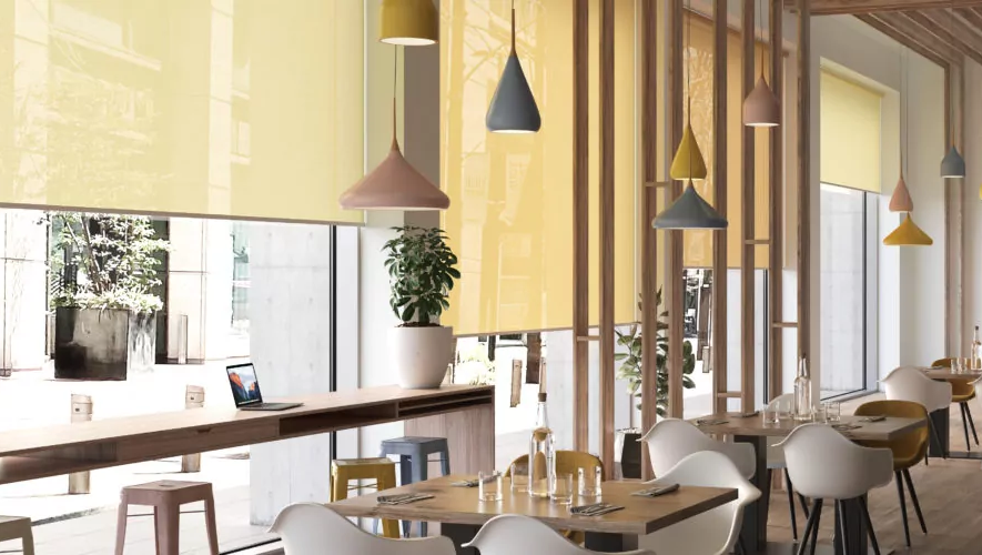 Mehrere gelbe Rollos schützen ein Restaurant vor Sonnenlicht und setzen gleichzeitig farbliche Akzente in dem Raum.