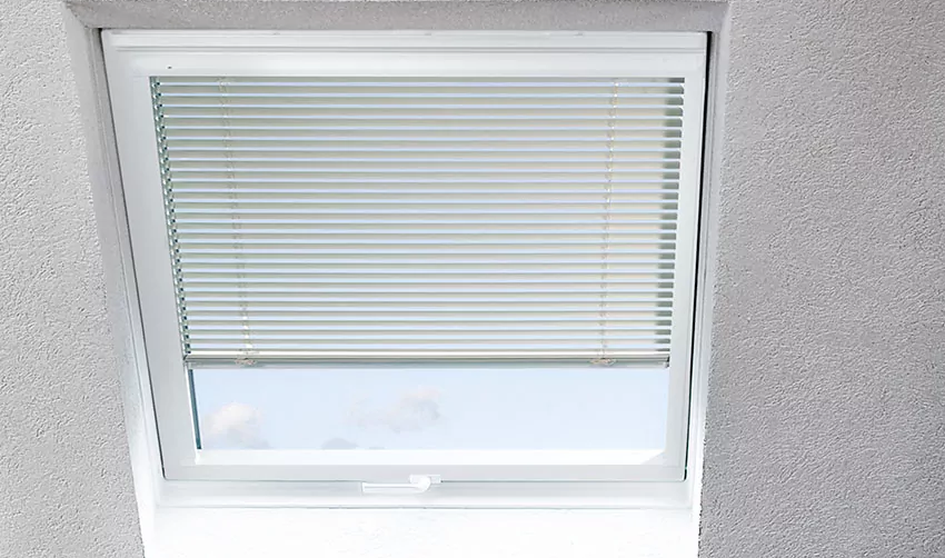 Ein quadratisches Dachfenster  mit einer Jalousie von MHZ mit horizontalen hellen Lamellen.