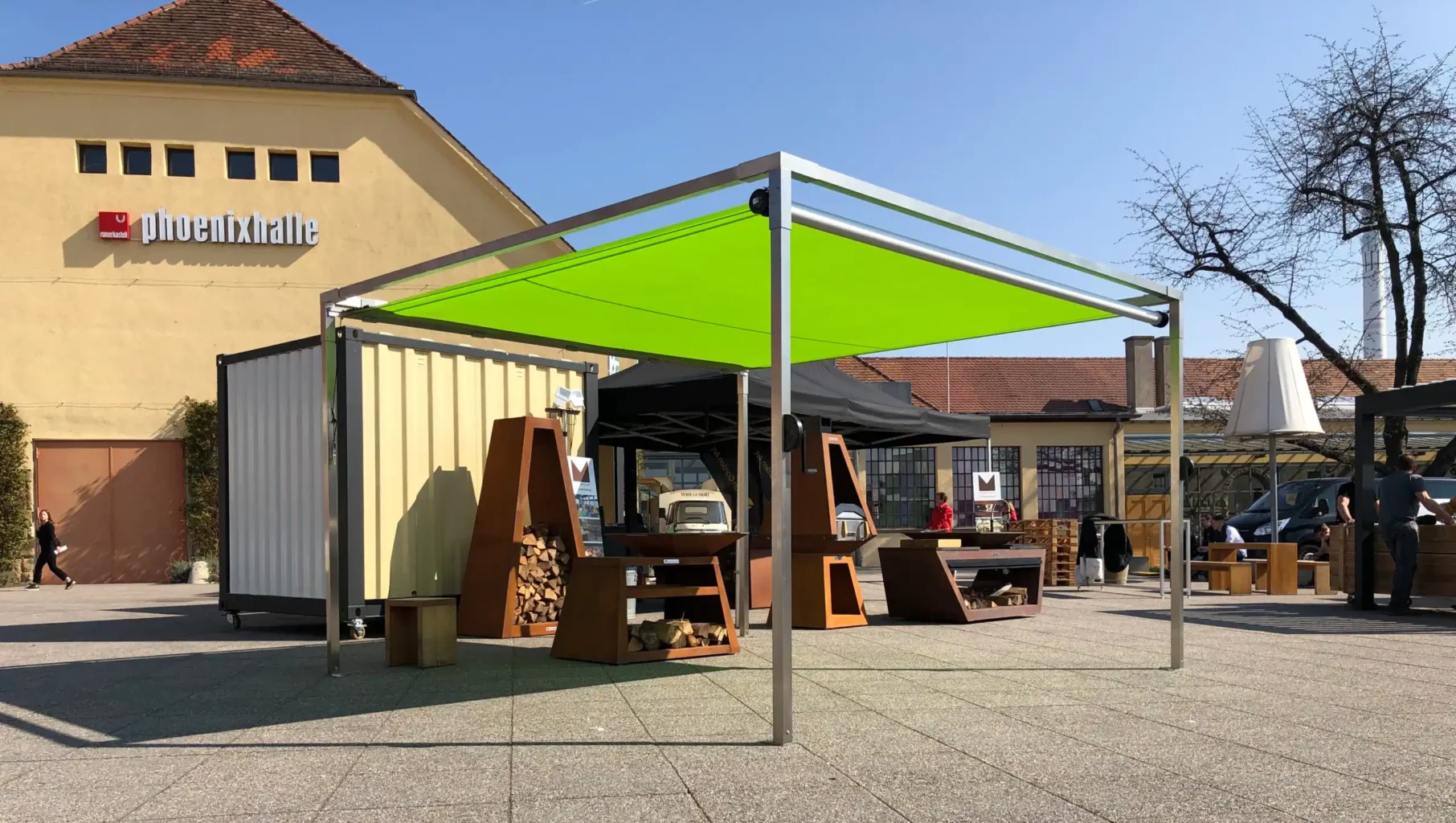 Ein freistehendes Shadesign Shade CUBE Sonnensegel, das ausgestellte Feuerholzlager beschattet.