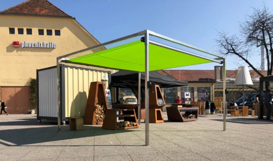 Ein freistehendes Shadesign Shade CUBE Sonnensegel, das ausgestellte Feuerholzlager beschattet.