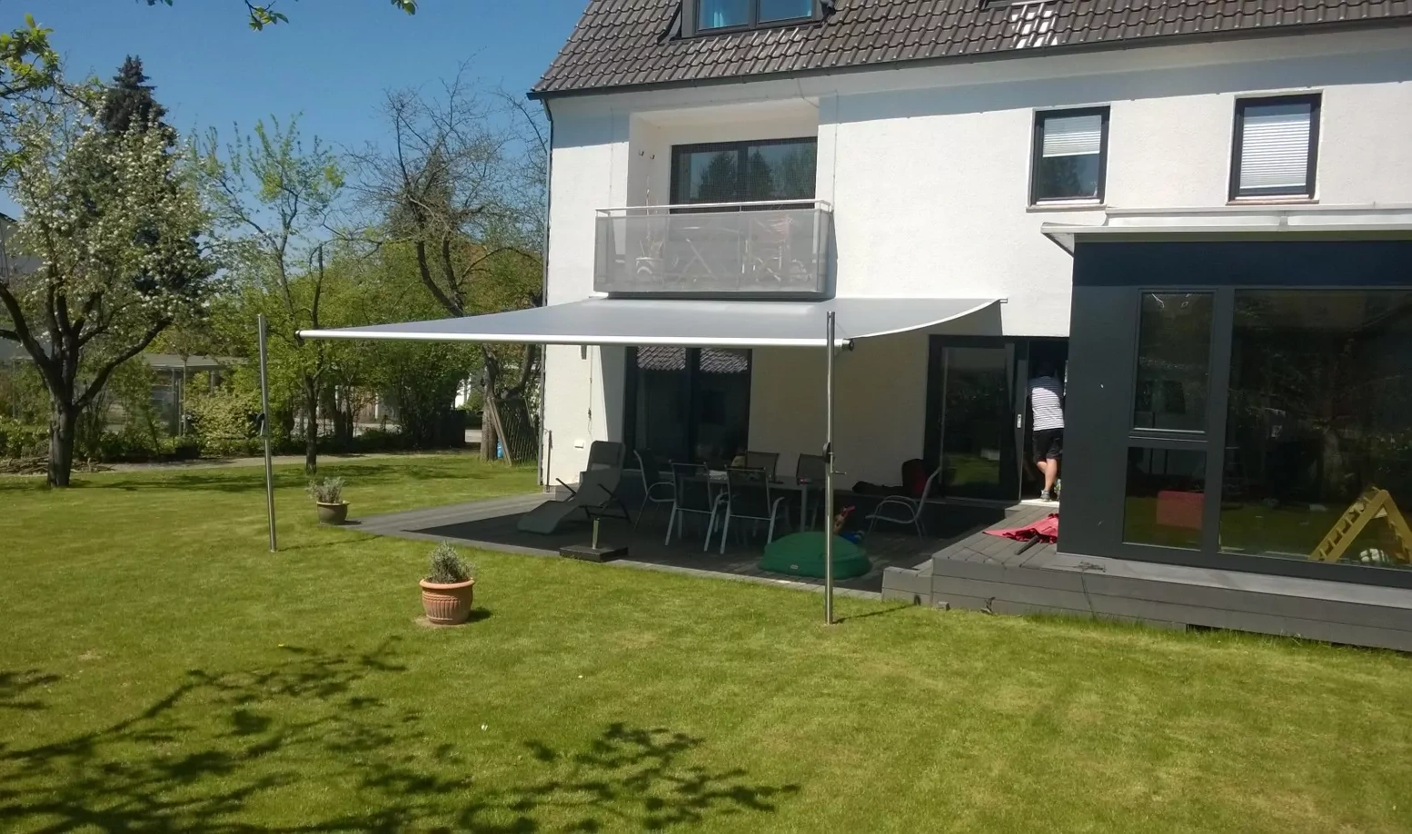 Ein gleichmäßig aufgespanntes Shadesign Shade INOX spendet großflächigen Schatten für Sitzgelegenheiten auf einem Sonnendeck an einem Haus.