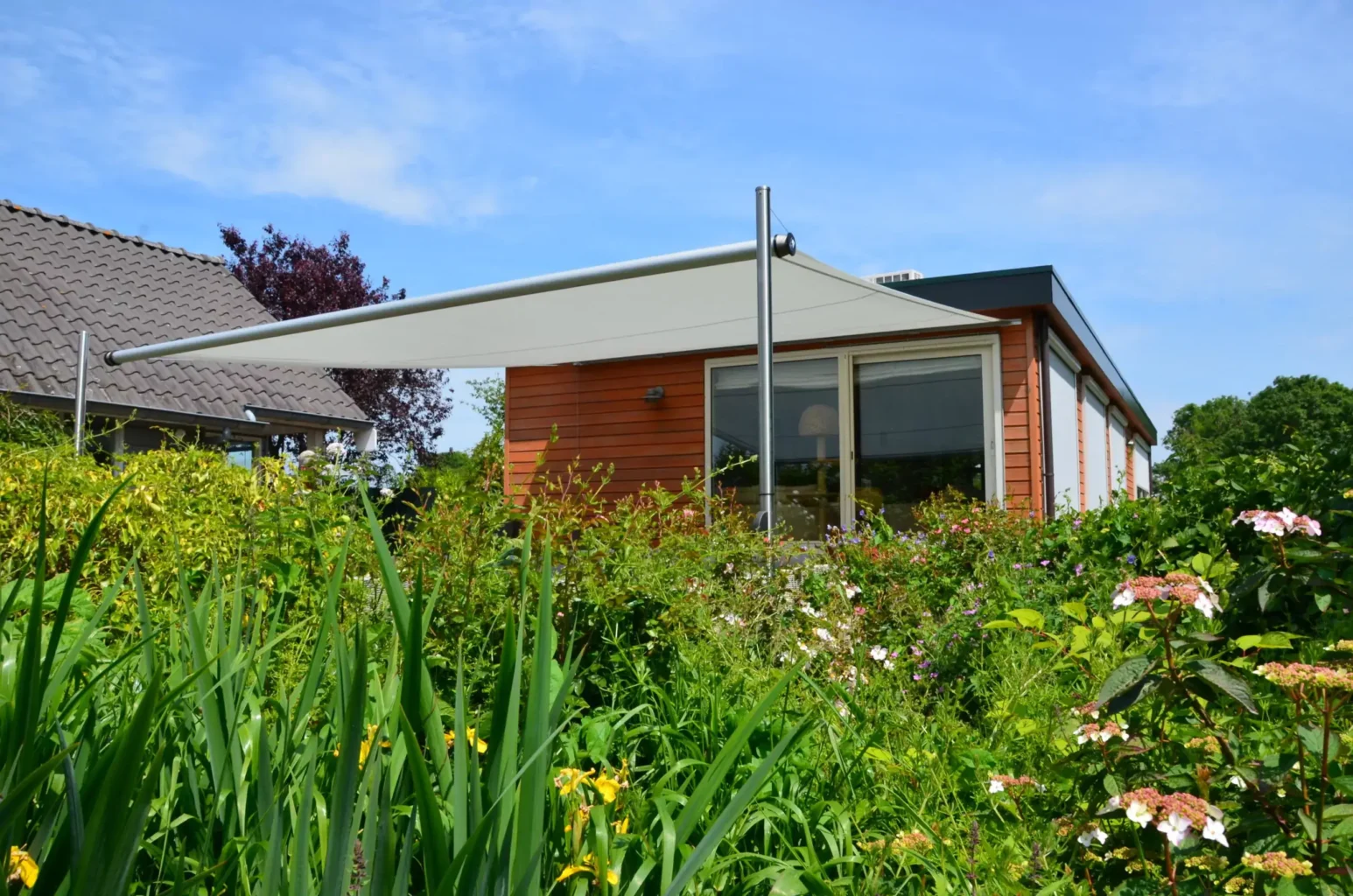 Das Sonnensegel Shadesign Shade INOX als Sonnenschutz vor einem Bungalow im Grünen.
