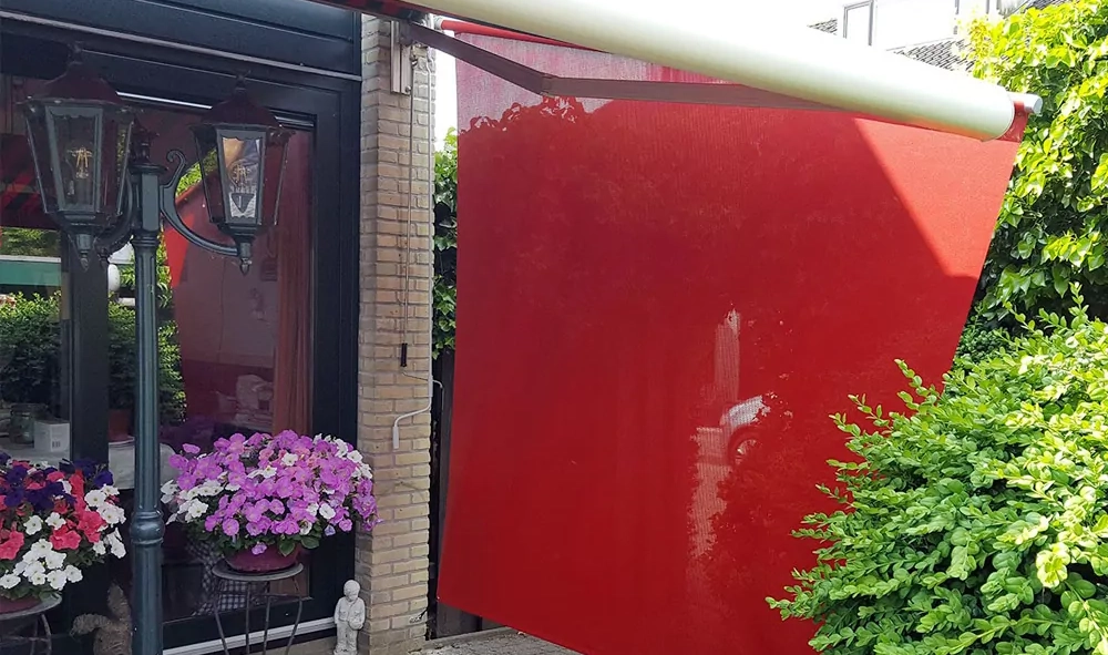 Ein aufgespanntes Sonnensegel Shadesign SKUGGI® in roter Farbe gegen seitliche Sonne und Wind.